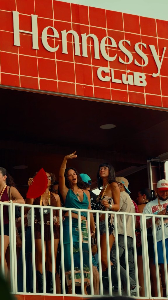 A group of people dancing below a large red tiled sign that says "Hennessy Clúb."