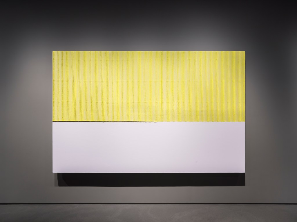A yellow and white painting by Park Seo-Bo hanging on a dark gray wall.