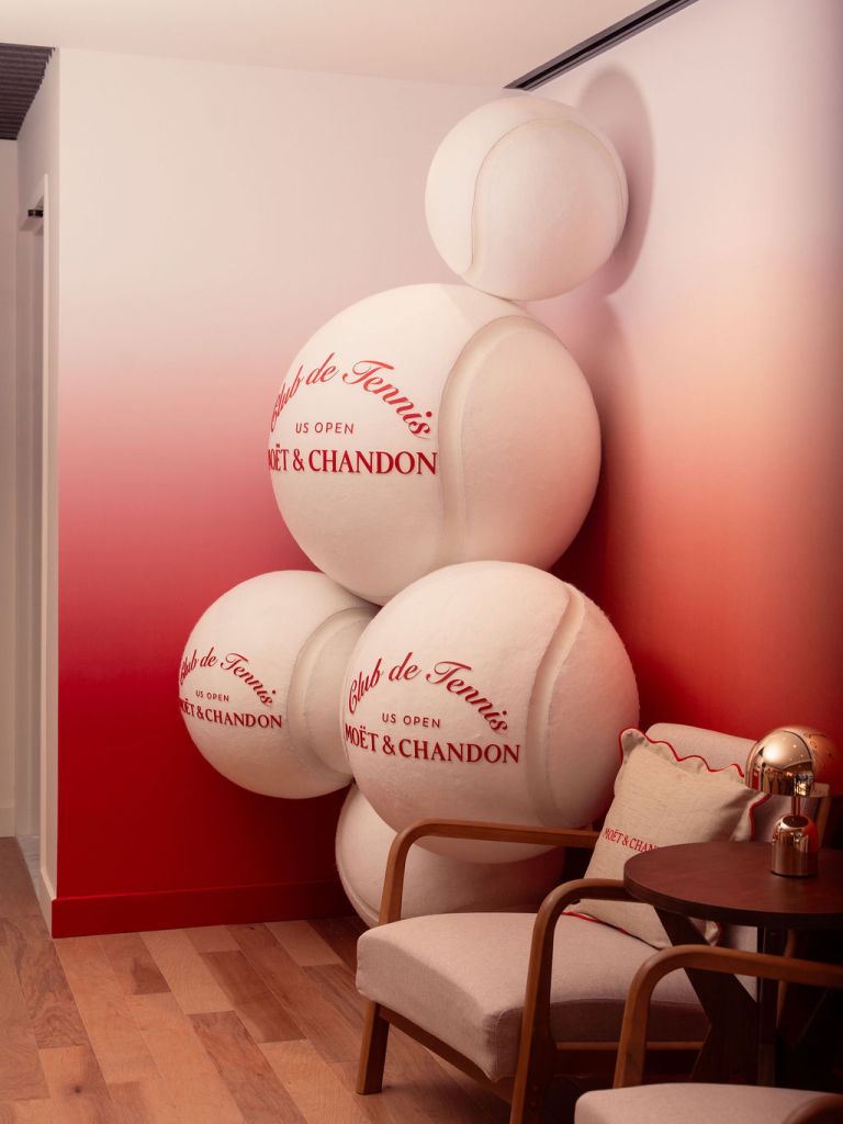 A display of oversized white tennis balls stacked in a corner against a red and white gradient wall.