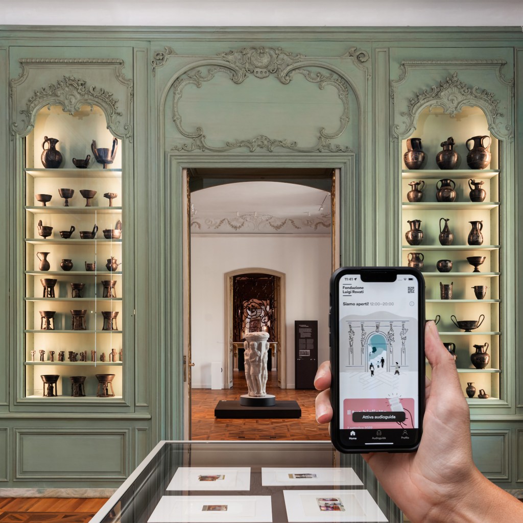 A view into green living room at the Fondazione Luigi Rovati, with a hand holding a phone with an app on the screen in the foreground.