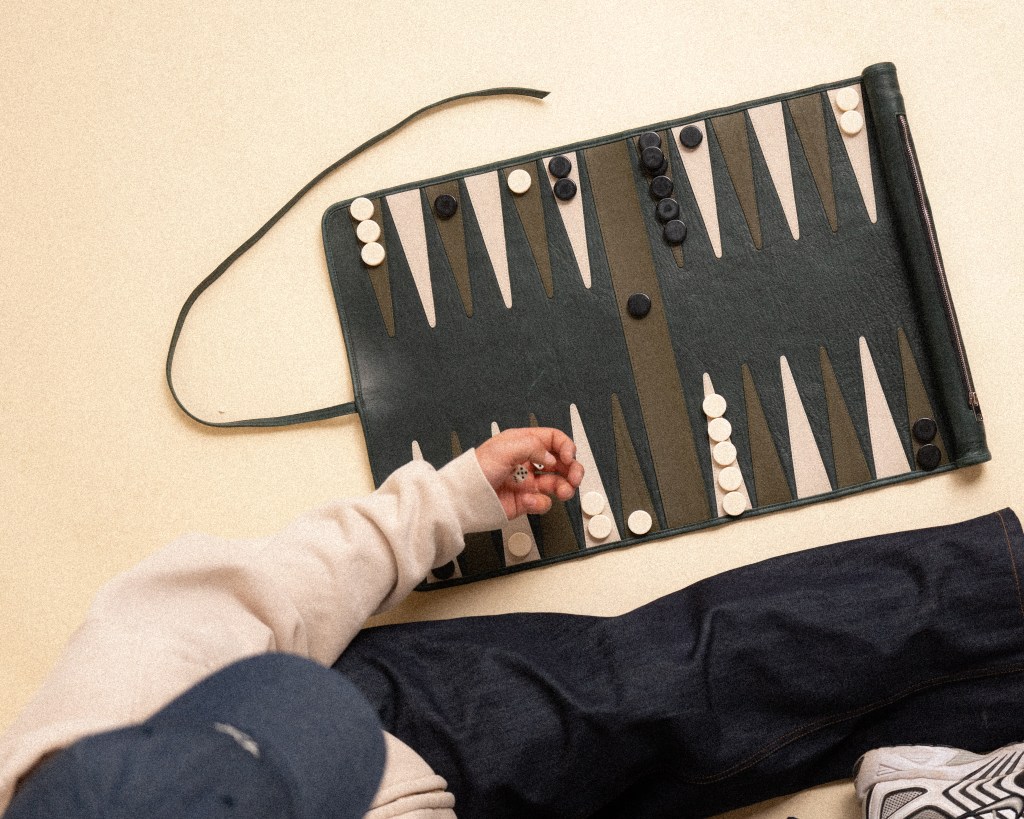 An overhead shot of the 1X backgammon board design, with a person wearing a sweater and jeans playing it.