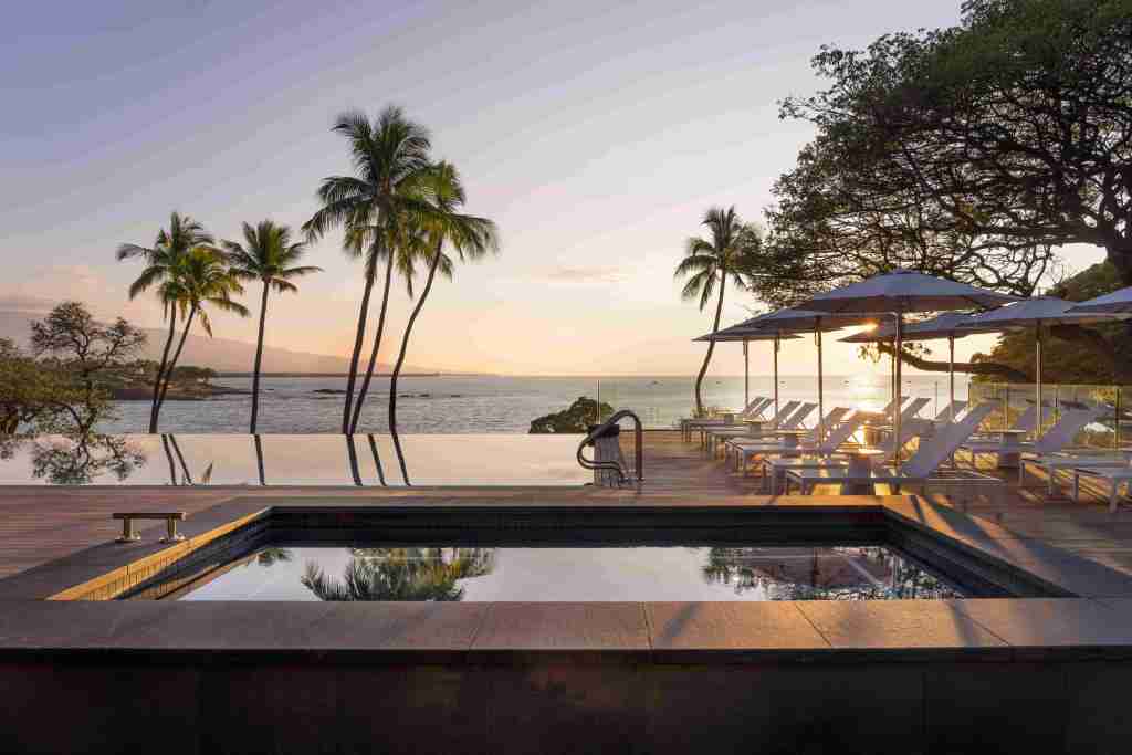 A view of the adult pool and jacuzzi at Mauna Kea Resort, looking out onto the sea at sunset.
