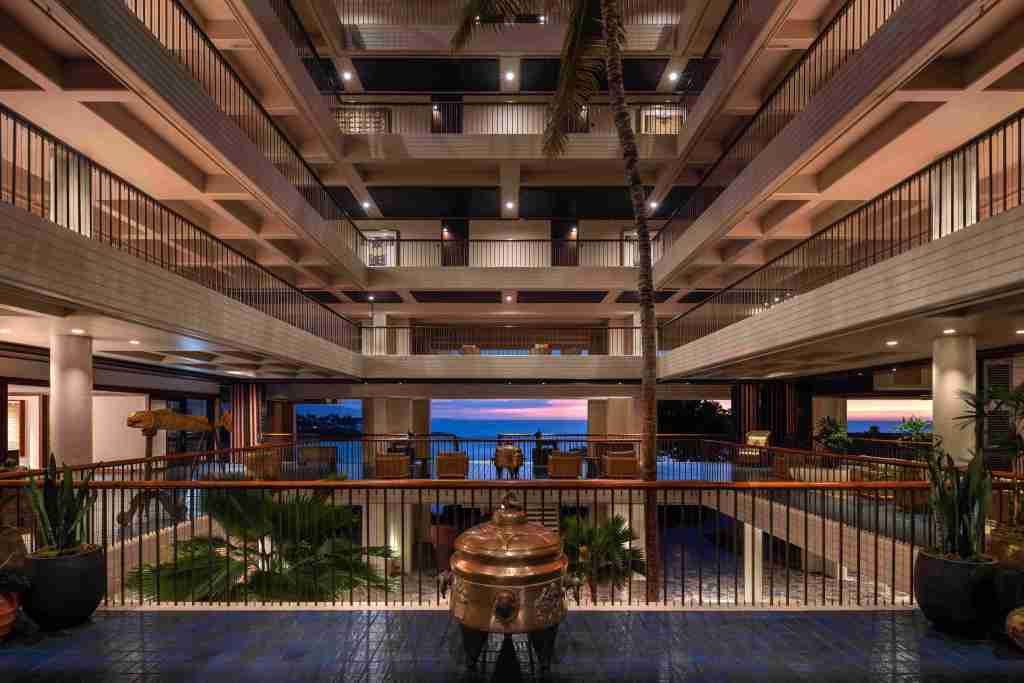 A view into the Mauna Kea Resort lobby with an open atrium that looks out onto the ocean beyond, shot at sunset.