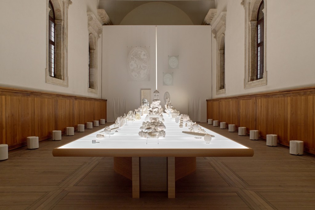 A long, illuminated white table with a variety of white objects displayed on top of it.