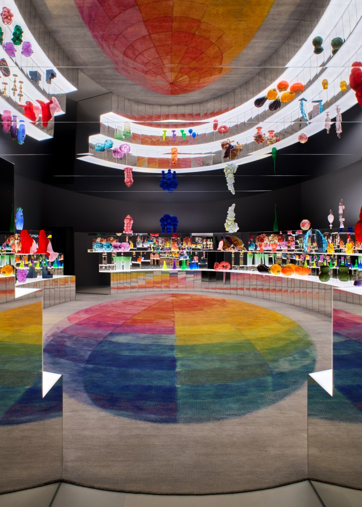 A room of colorful items arranged in a circle, with a rainbow floor in the middle and a mirrored ceiling that reflects everything below it.