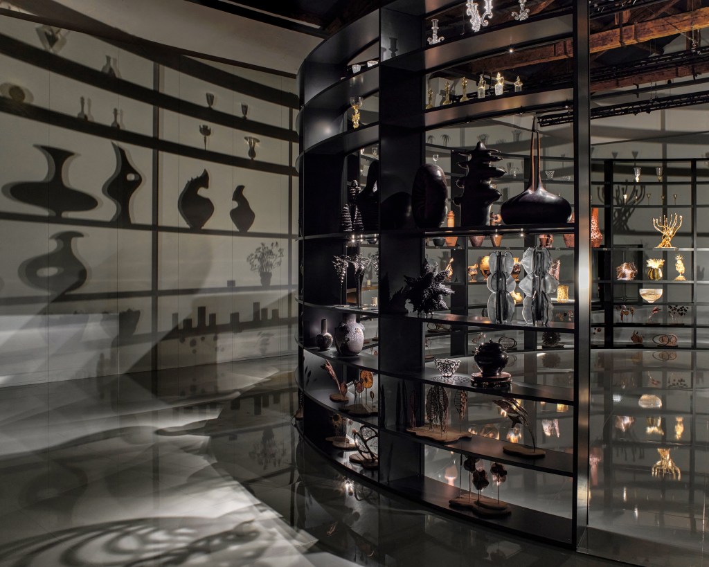 A large circular shelf of objects, rotating in a dark room and casting shadows on the walls.