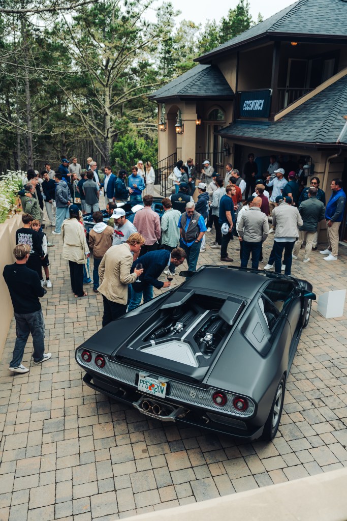 A photo of a crowd at Monterey Car Week looking at a black car in a driveway.