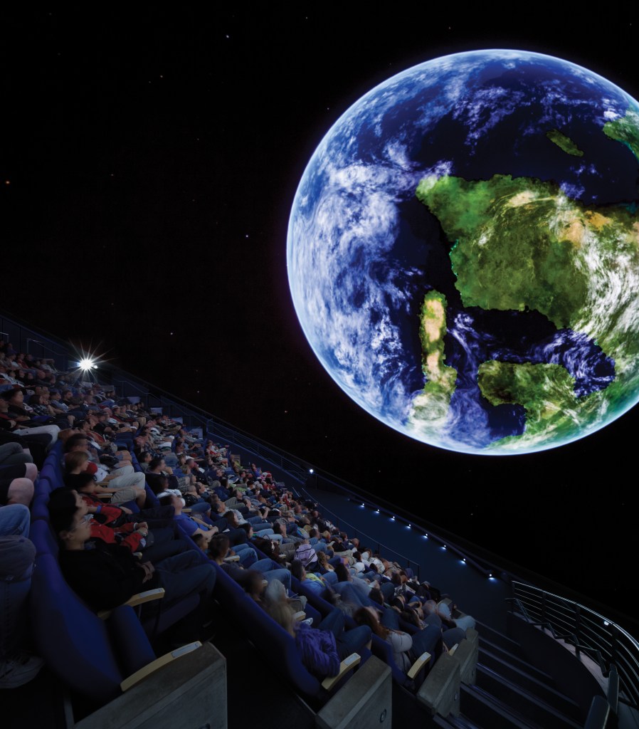 A view of the planetarium at the California Academy of Sciences with a large image of earth on the screen in front of a crowd.