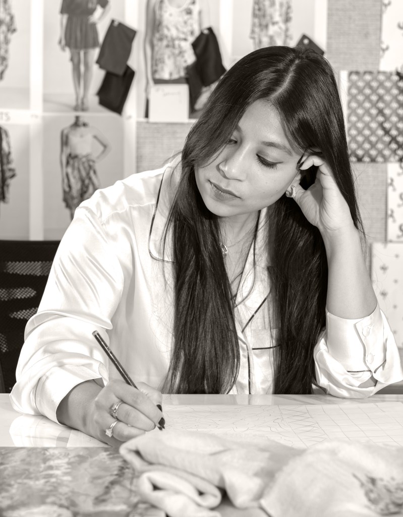 A black and white photo of Shwetambari Mody looking down at a table as she hand draws designs.