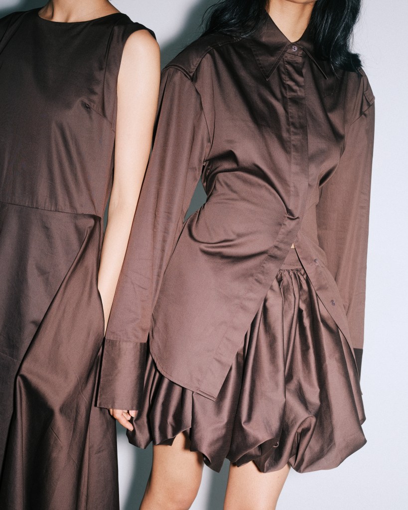 A tight shot of two models standing close together wearing different brown outfits.