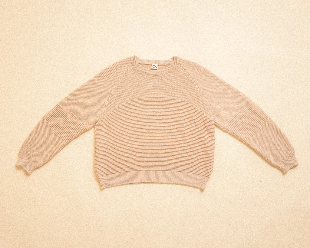 A tan sweater lies open on a beige surface.