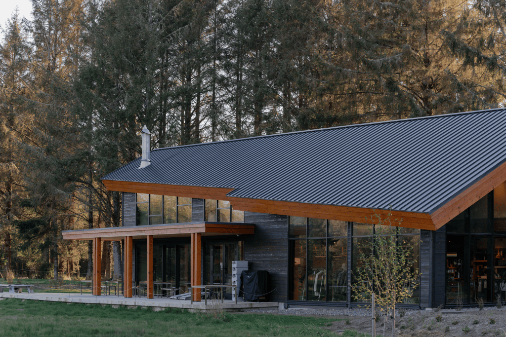 A minimal low-slung wooden building with a slanted metal roof and woods behind it.