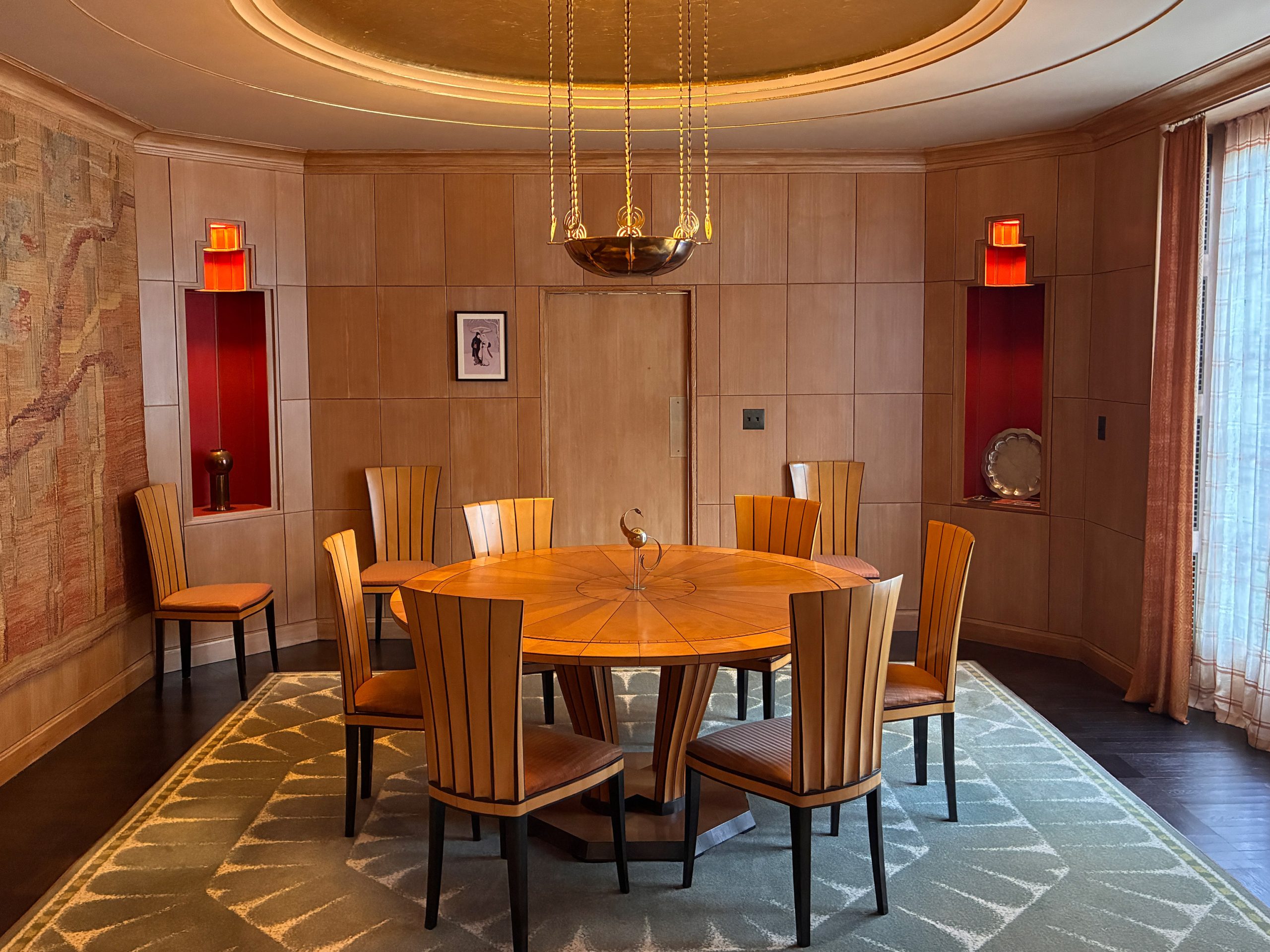 A dining table with a gold leave dome above it and an octagonal rug.