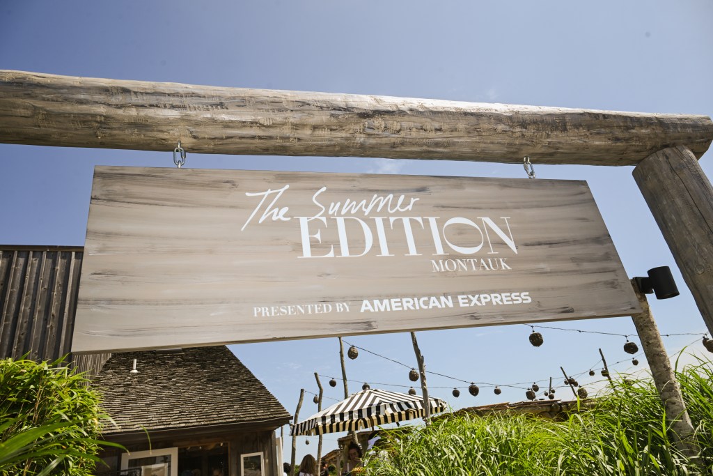 A drift wood sign that says "The Summer EDITION MONTAUK, presented by American Express" in white letters with a blue sky background.