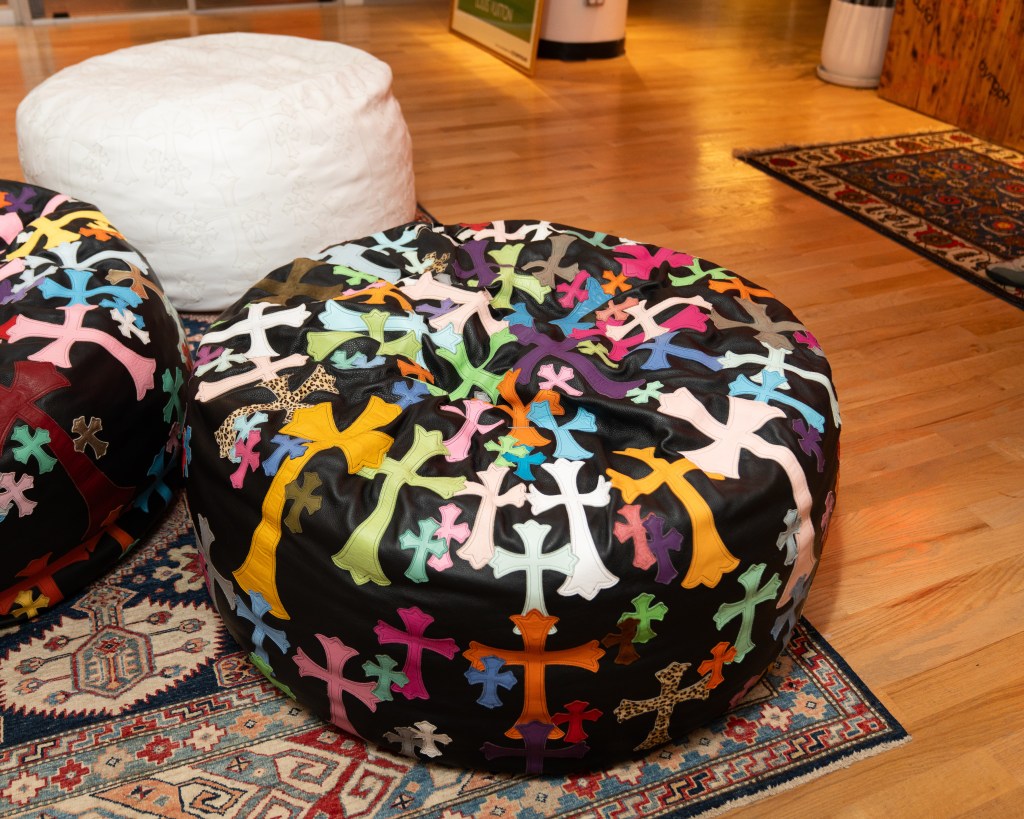 Three leather ottomons sitting on a Persian rug; two of which are black with colorful crosses stitched onto the surface.