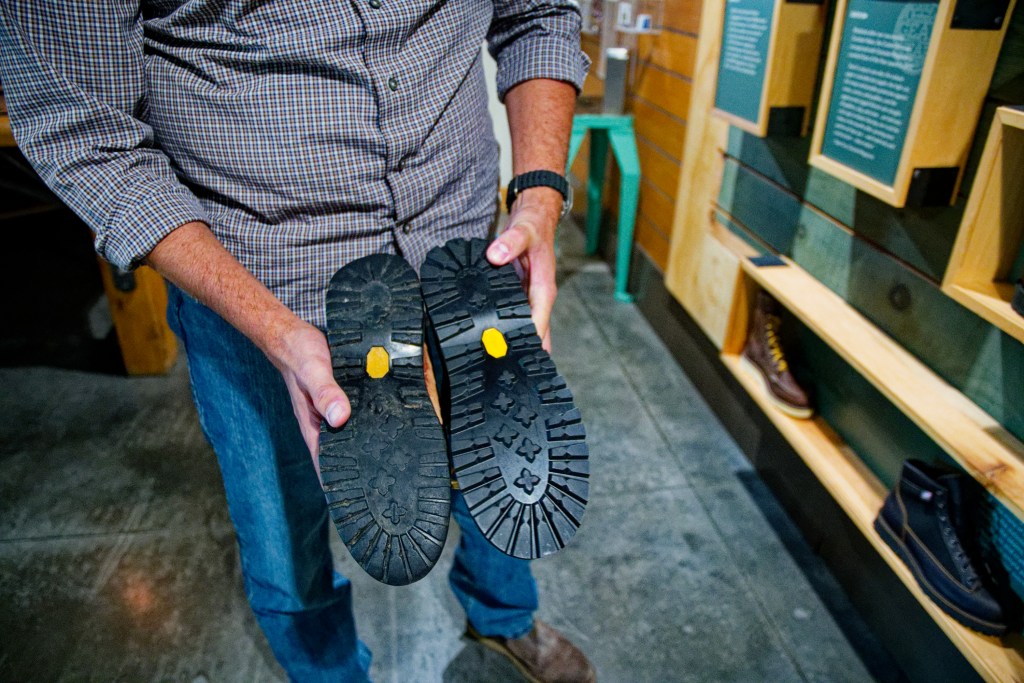A pair of hands holding a Danner boot upside down to show the outsole; one is worn down and one is brand new.