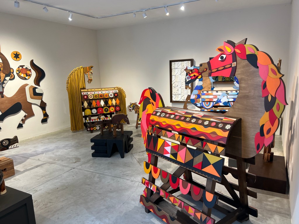 A room with a variety of geometric, colorful painted horse artworks displayed. 