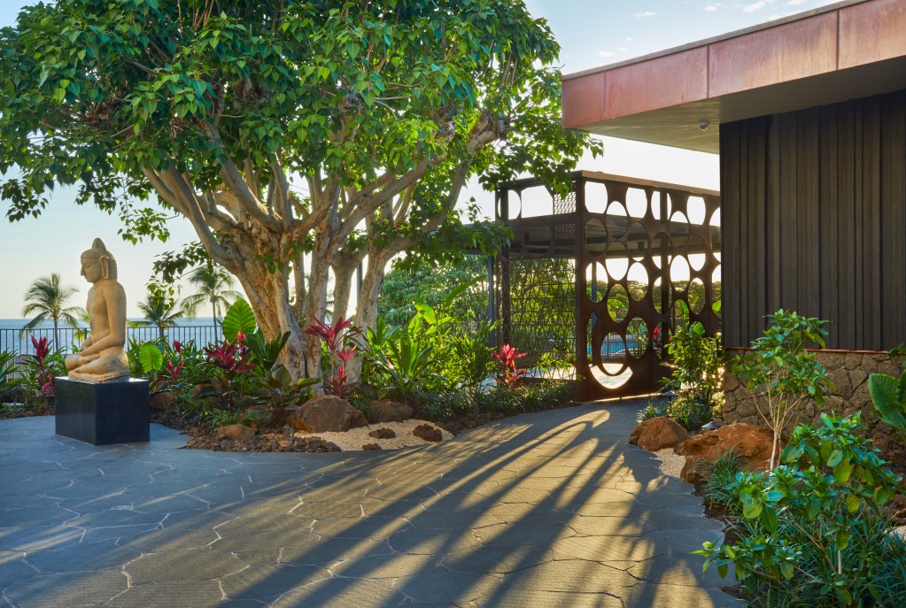 The exterior of the Mauna Kea Resort spa with a large Buddha statue displayed outside the path.