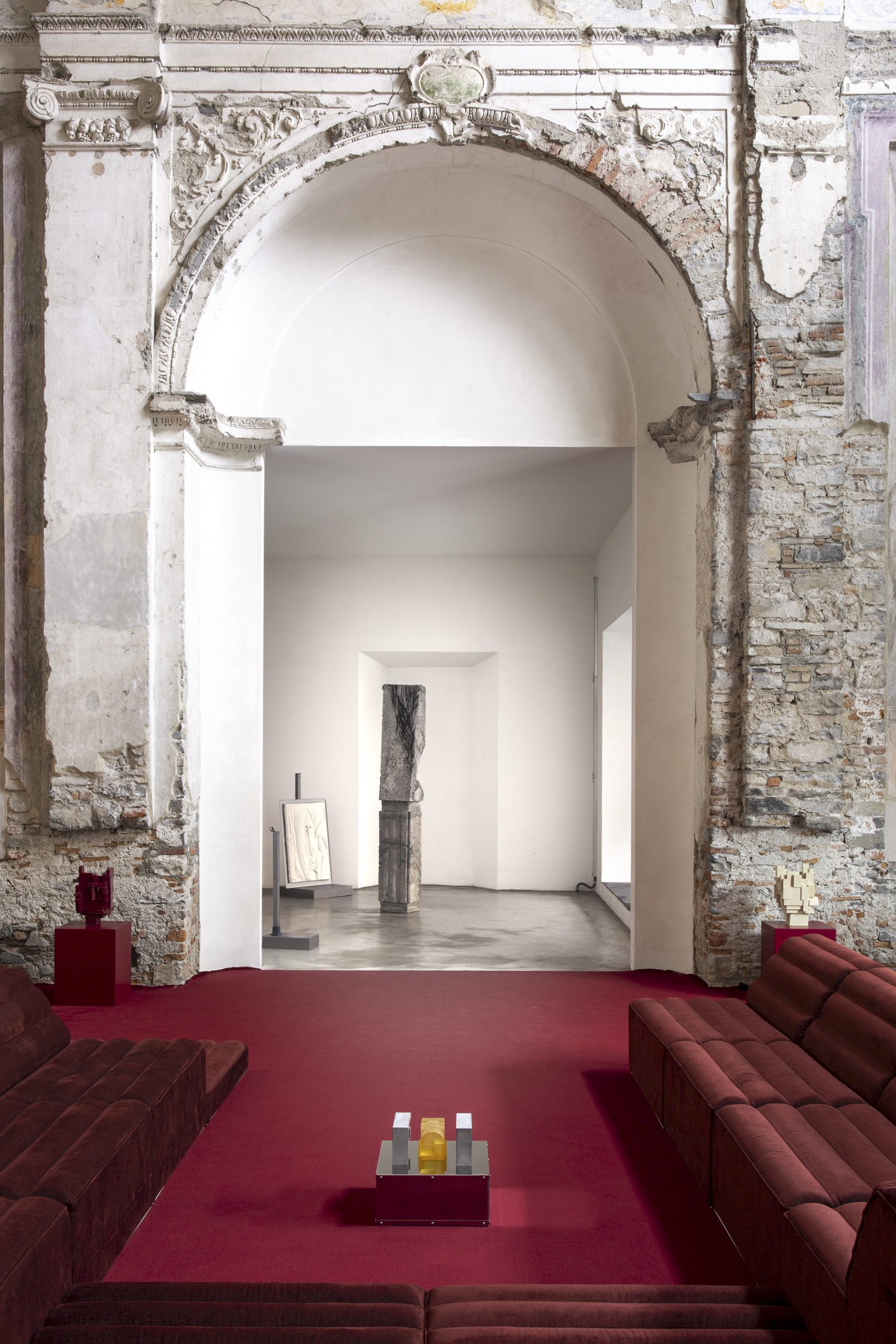 A red carpeted room looking out towards a large marble archway, where sculptural artworks are displayed.