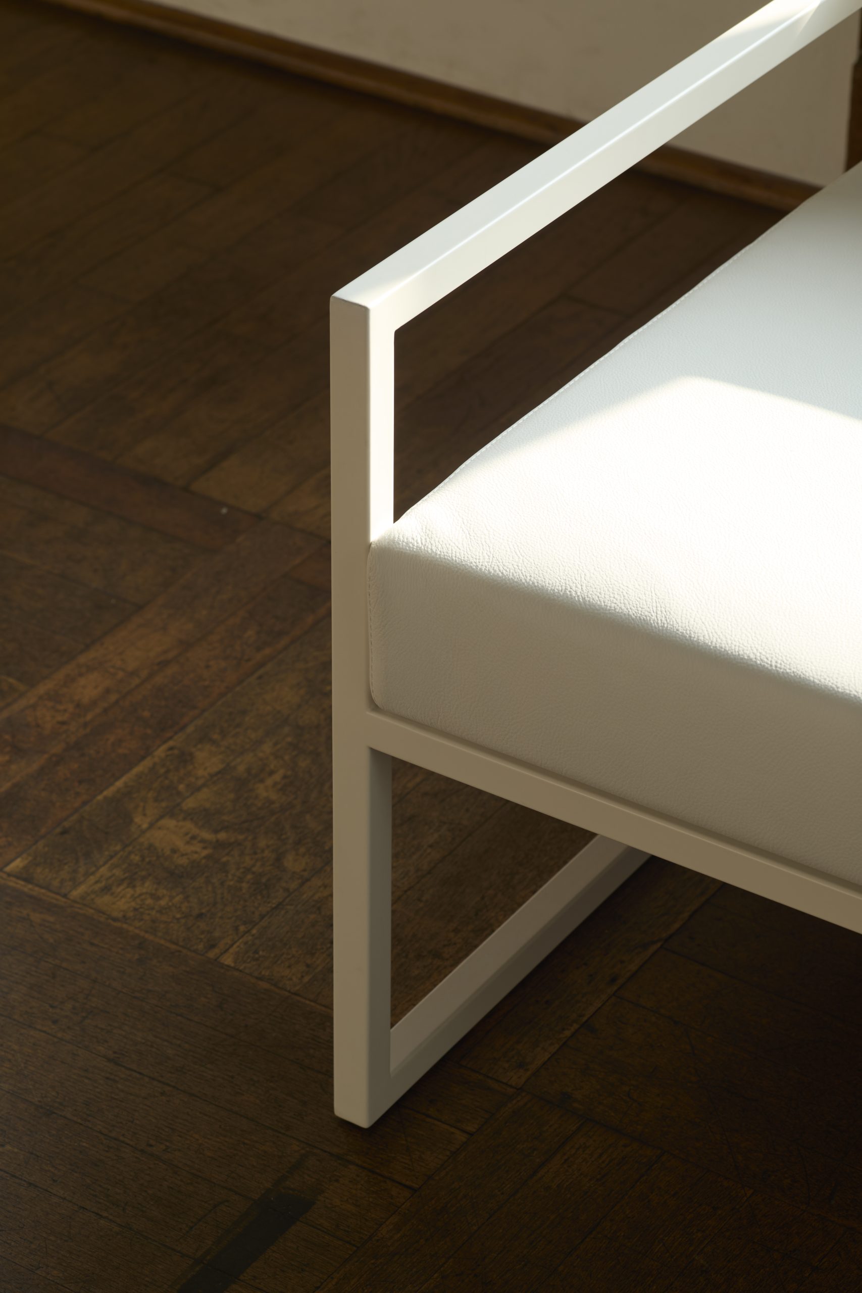 A detail of a minimal white arm chair on a wood floor.