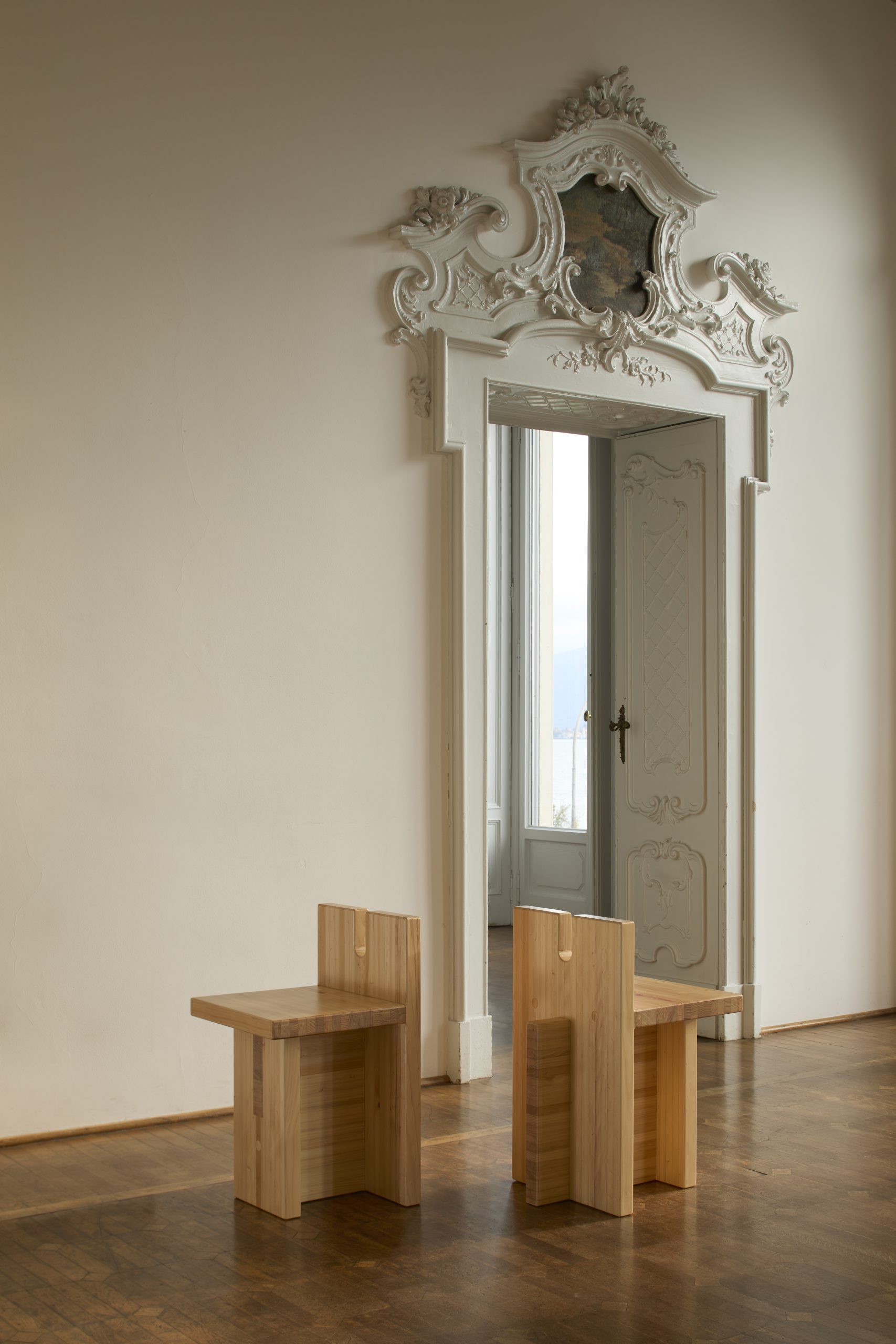 A pair of simple wood chairs sit in an ornate, historical room.