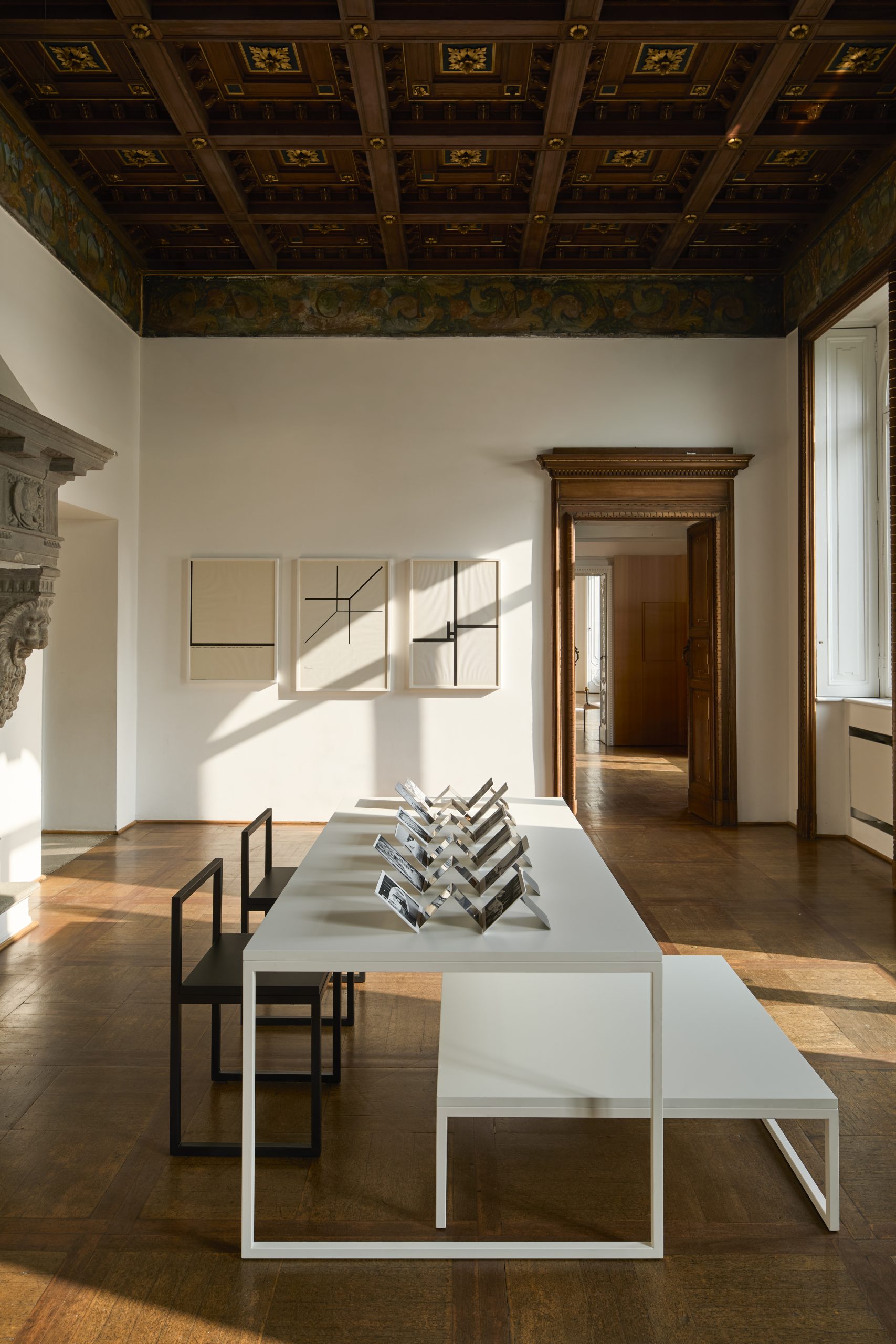 A large room with white walls and a wood floor, displaying paper ephemera on small easels on a long white table.