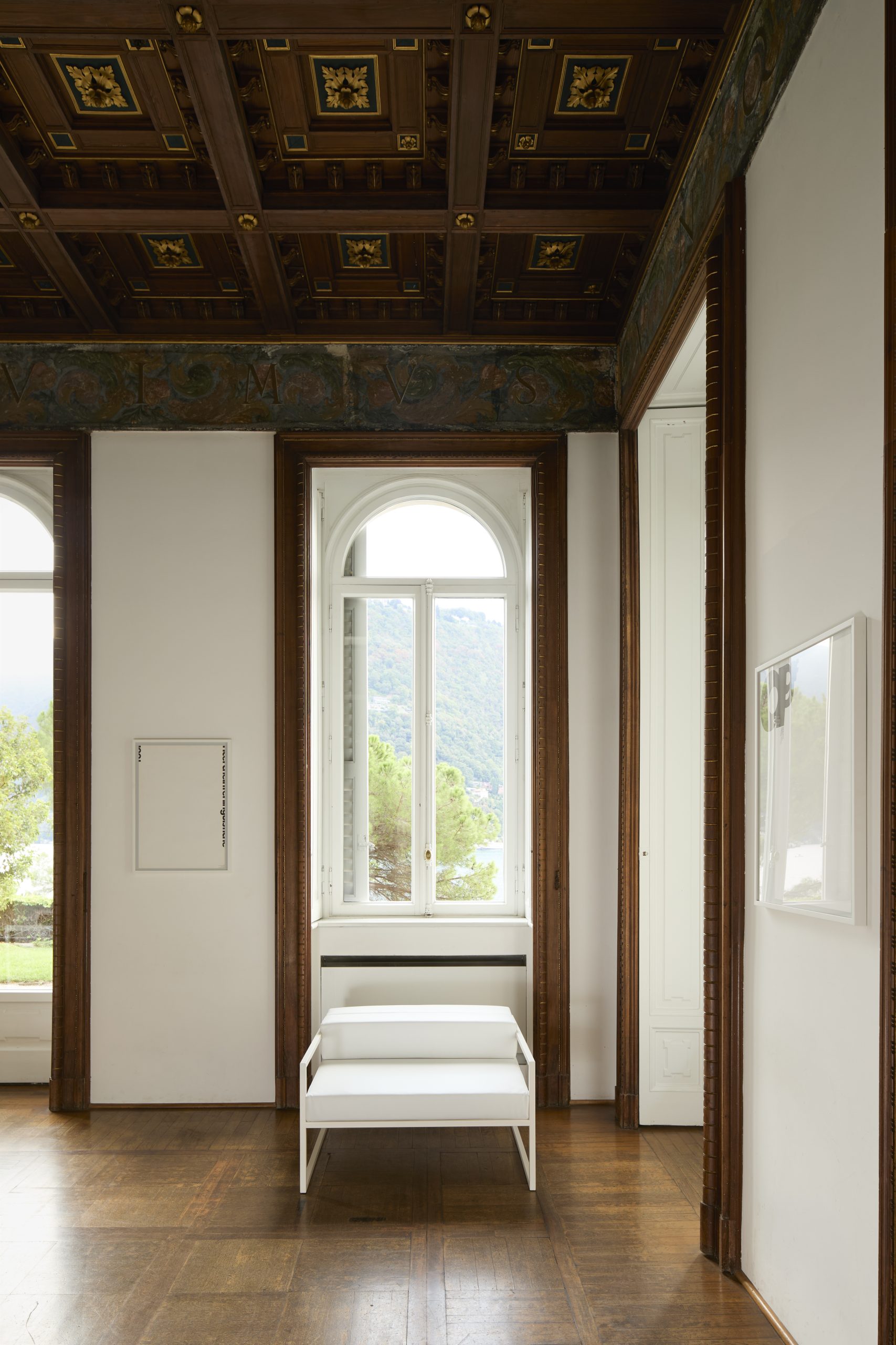 A minimal white armchair sits in front of a tall, ornate window.