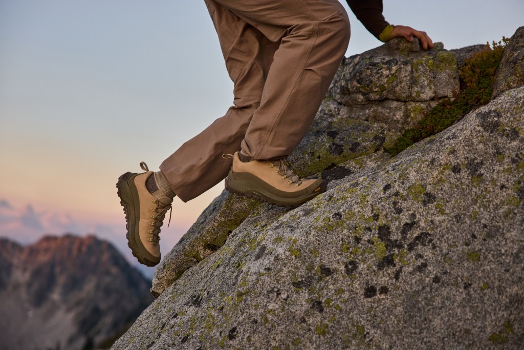A figure scrambling up a rockface, wearing a pair of Danner shoes with a sunset in the background.