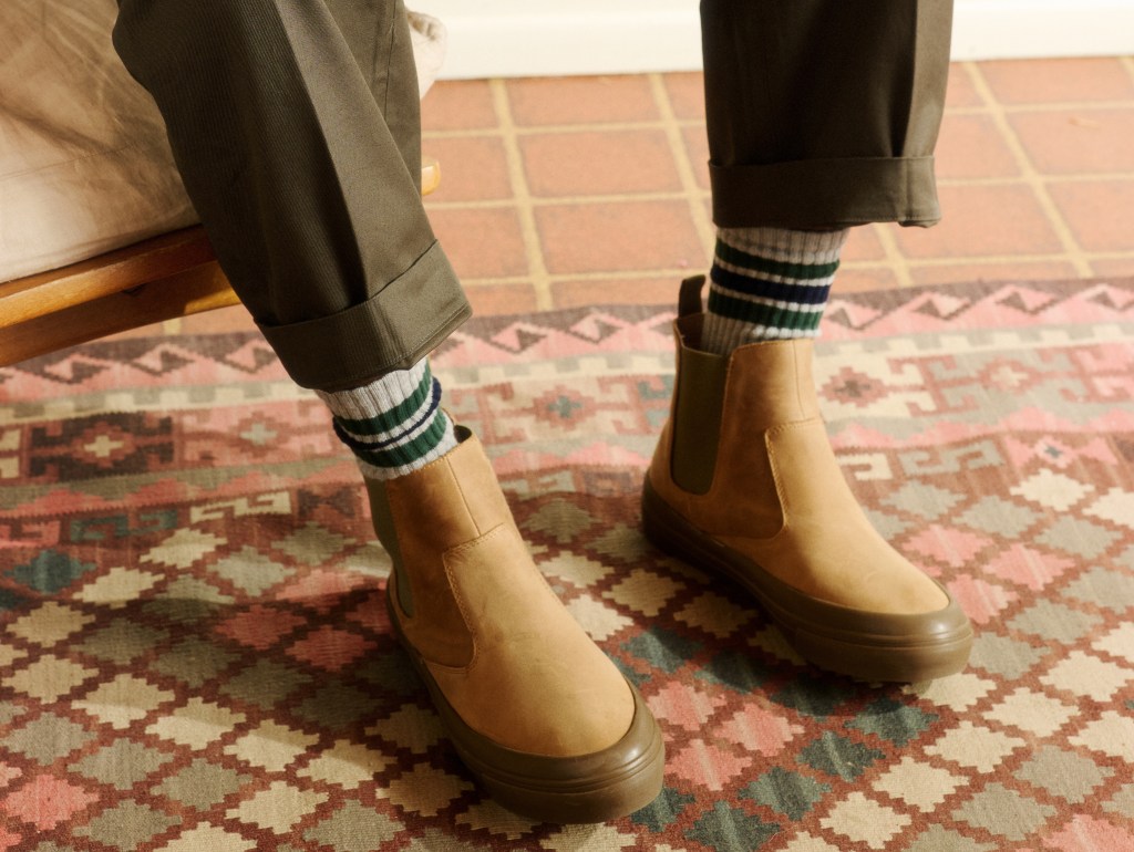 A cropped shot of a man's legs, wearing olive green pants, striped socks and a pair of tan Beyond and Back boots.