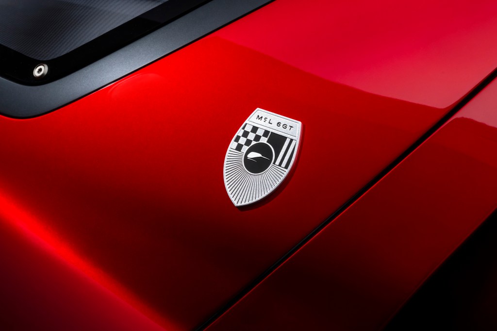A tight shot of a silver McLaren McL 6GT emblem on a smooth, curved red car exterior.