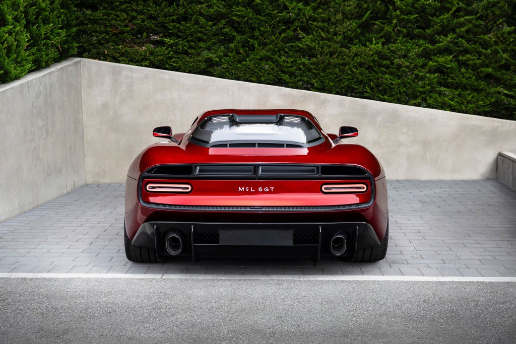 The back of a red McLaren McL 6GT parked in a driveway with an angular concrete corner in front of it. 