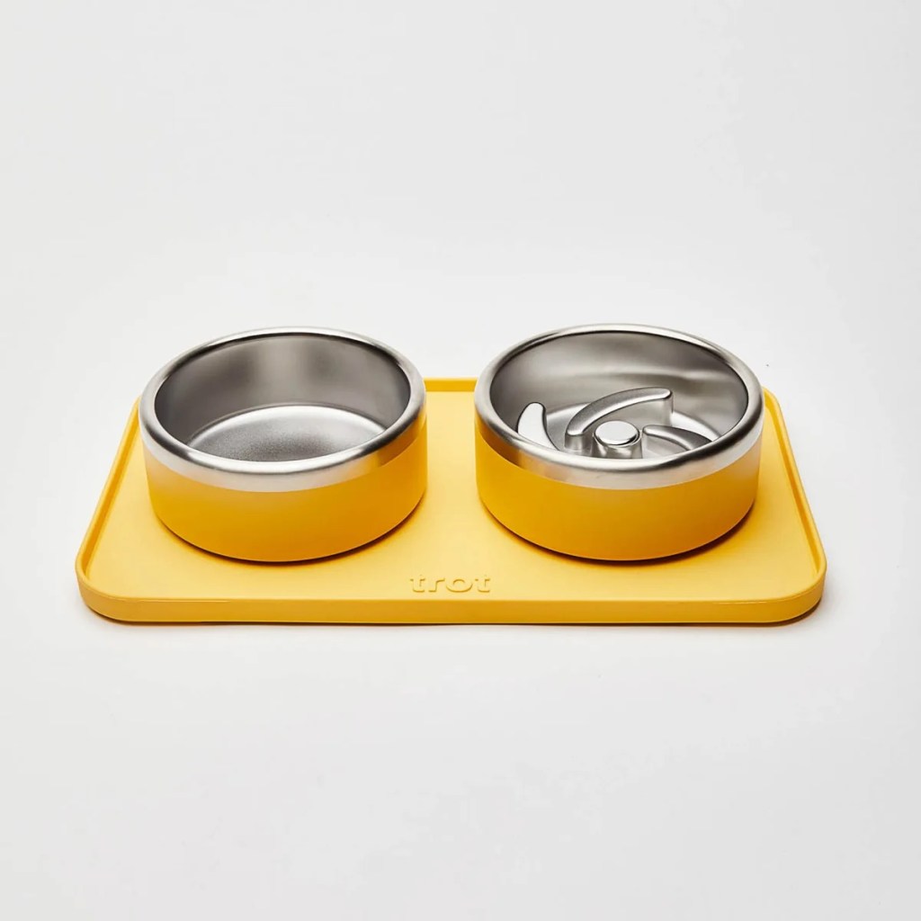 Trot's water bowl, puzzle food bowl, and mat, shown in yellow