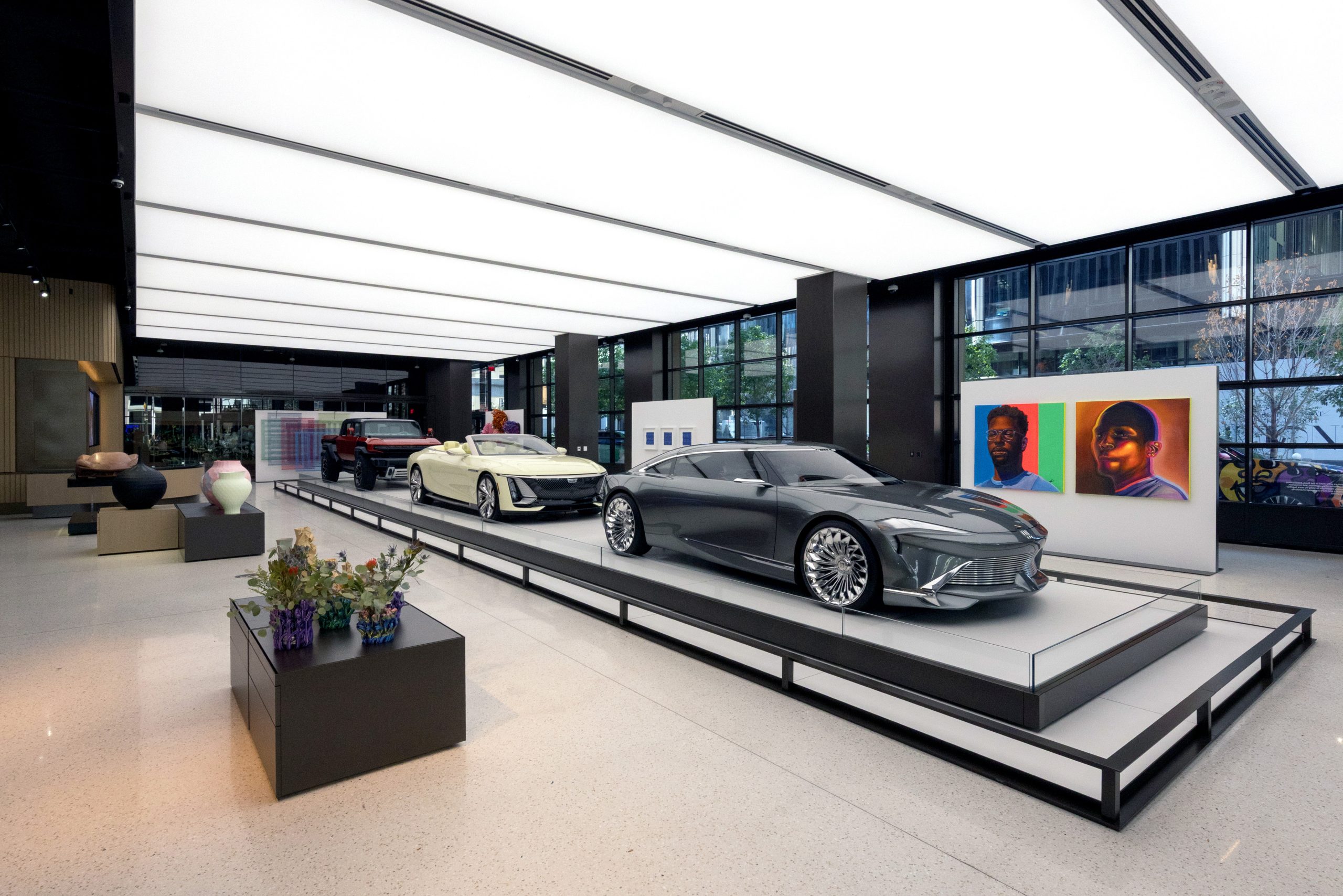 Three GM cars parked on platforms in a vast interior room with artwork surrounding them.
