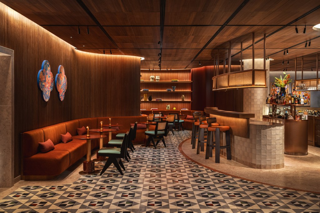A room with curved wood panel walls, colorful tiled floors, and deep orange sculptural furniture with a bar to the far right.