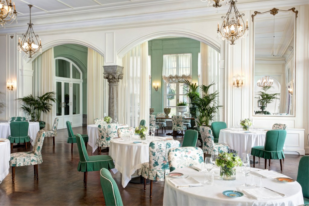 A dining room at Florio Restaurant with tall arched ceilings, dark wood floors, and a green, white and floral motif in the chairs and table linens.