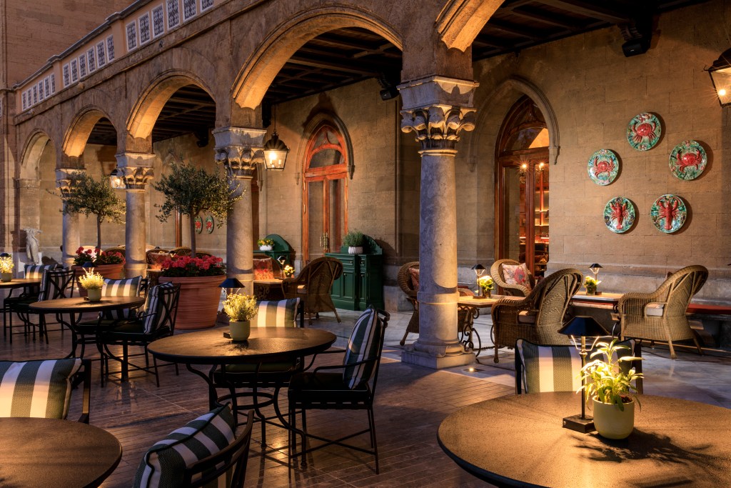 A grand bar room with Belle Epoque archways, dim lights, multiple tables and seating options, and an ornate balcony above.