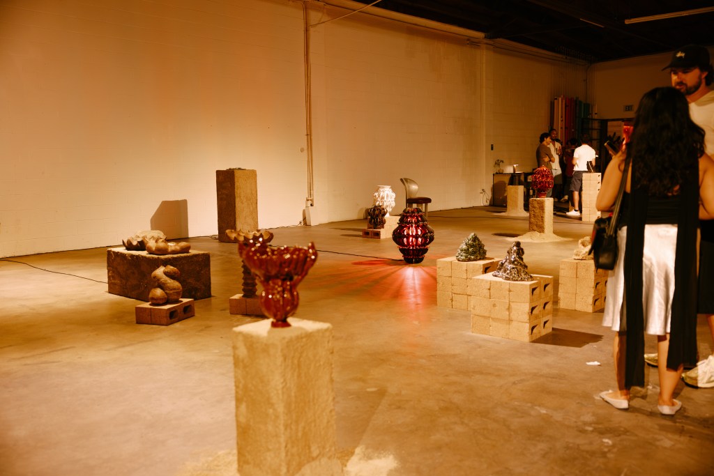 A large, dimly lit gallery room with several pedestals placed around the space, exhibiting sculptures.