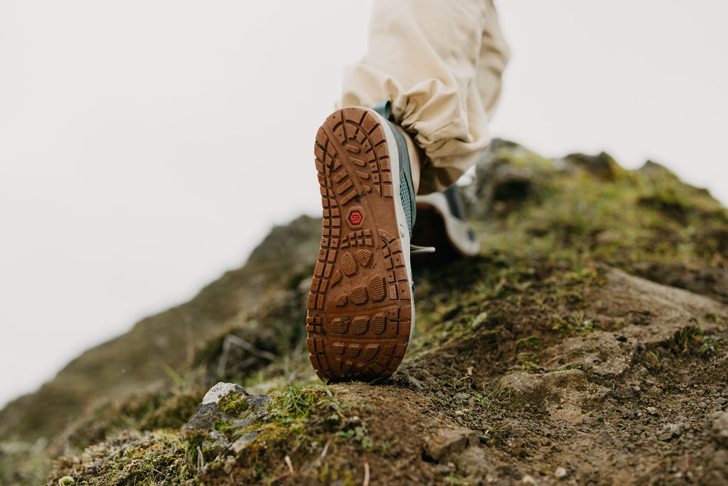 A pair of feet scrambling up a rock, showing the sole of the Astral Designs Techyak shoe with a red dot on it.