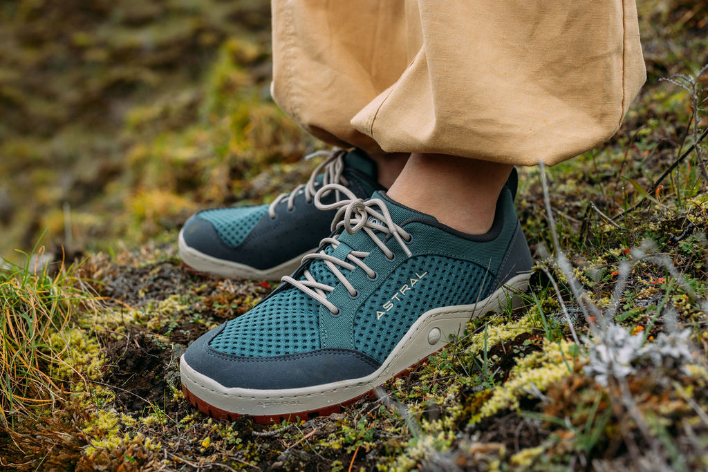 A pair of feet wearing a pair of dark teal Astral Designs Techyak shoes, standing on a moss surface.