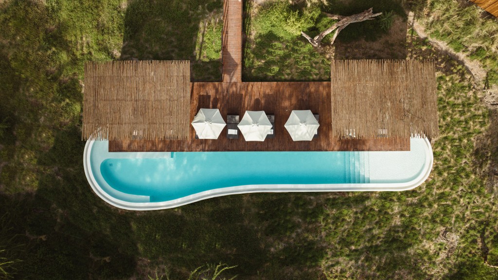 An aerial view of the salt water pool at Kitirua Plains Lodge with a thatched roof patio and three umbrellas in the middle.