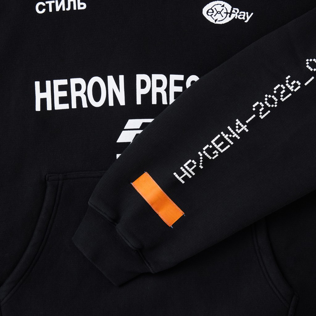 A tight crop of a black Heron Preston hoodie with a sleeve folded over, showing an orange tag and white text running up it.