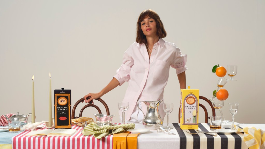 Laila Gohar standing behind a table with striped tablecloths, sculptural tabletop settings and two bottles of Highland Park whisky.