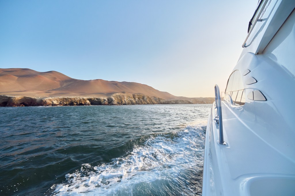 A view looking off the deck of a yacht on the water and the rolling desert hills to the left.