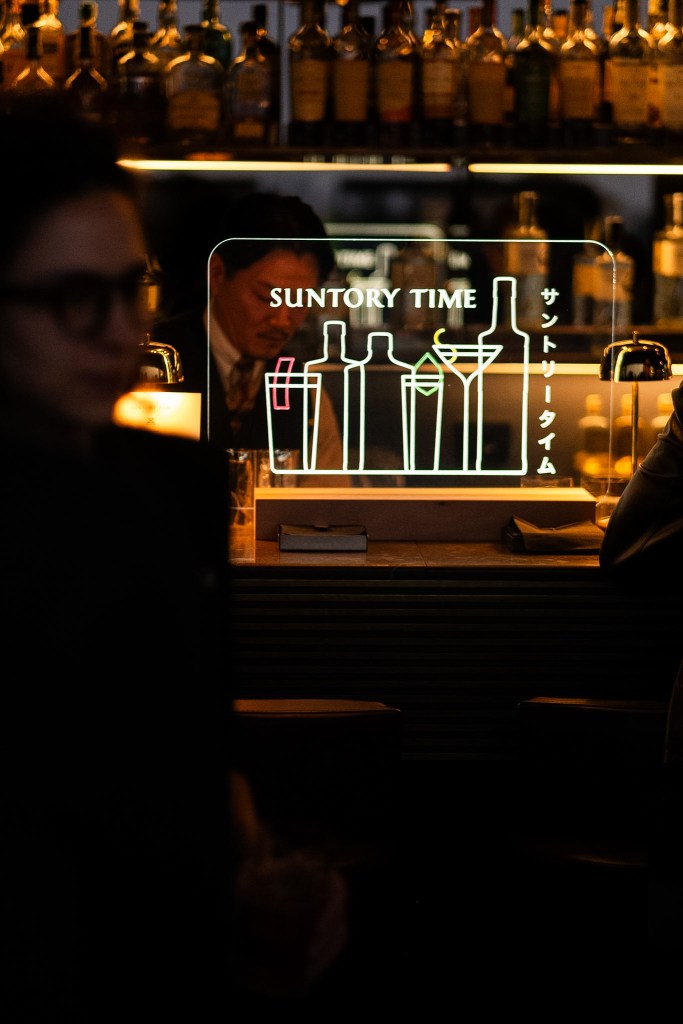 A neon sign that says "SUNTORY TIME" sitting on a dark bar.