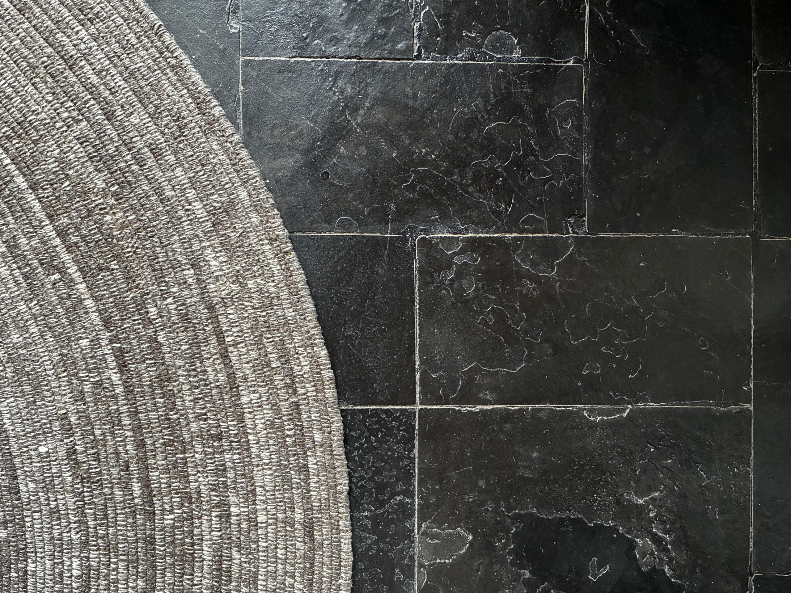 A detail of a Mazeras stone floor with a braided jute rug on the left.