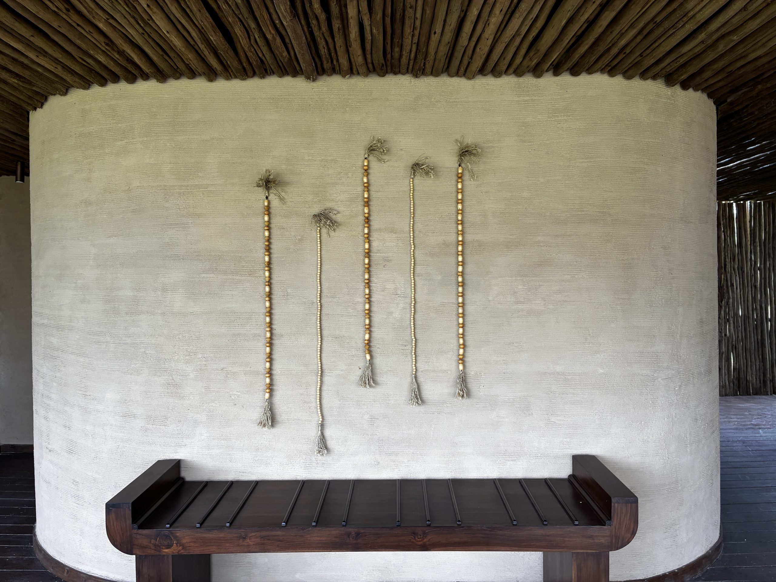 A textured white wall with five beaded strings handing above a bench.
