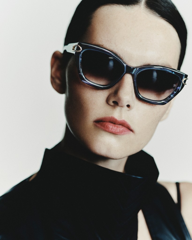 A model with red lips and slicked back hair wear a large pair of sunglasses.