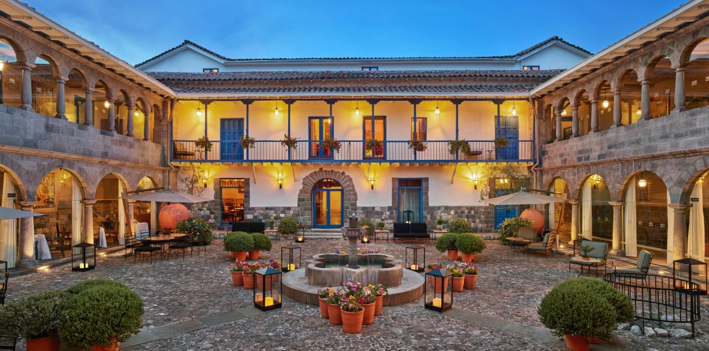 The two-story courtyard at Palacio del Inka with a central fountain, tables and chairs, and potted plants. 