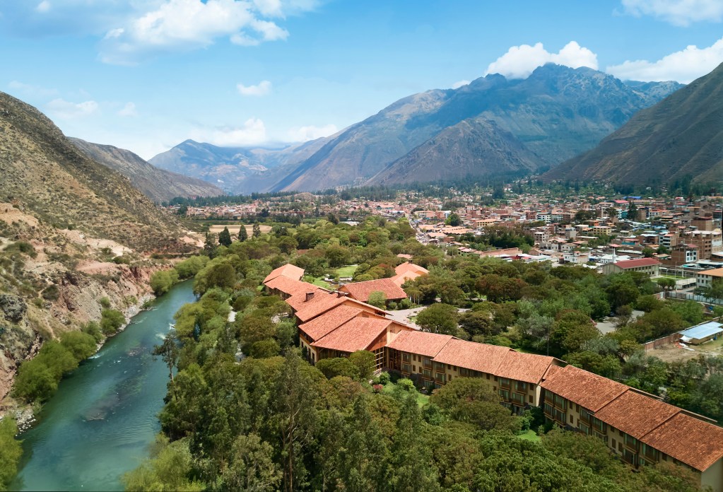 An aerial view of Tambo del Inka with a river to the left and the Andes mountains in the background.