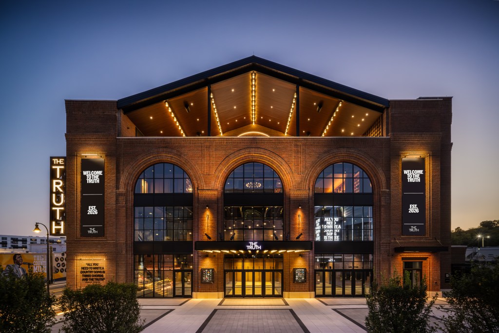 An exterior view of an illuminated, large brick building with signage that reads "The Truth Est. 2026."